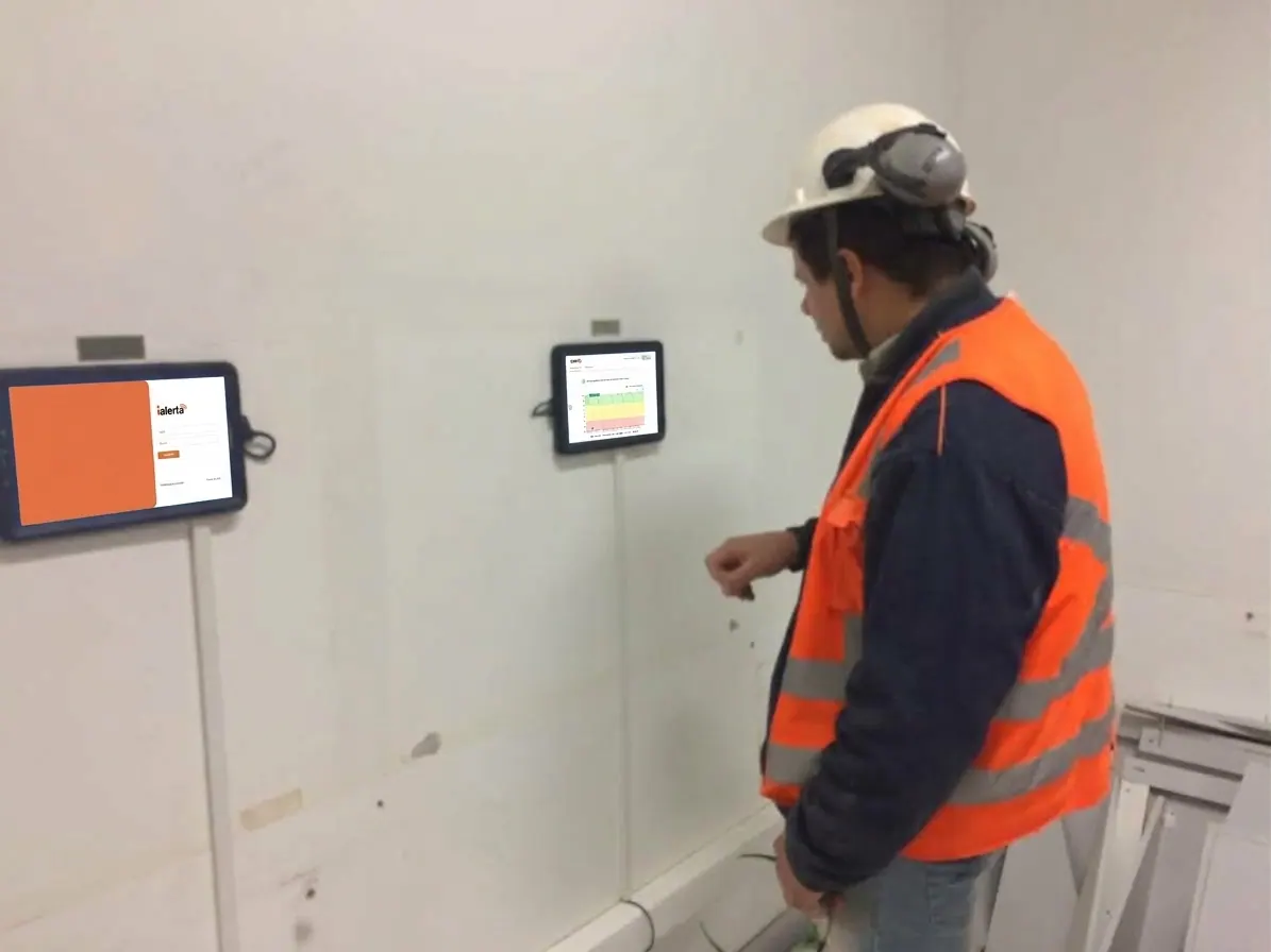 Trabalhador de capacete usando o tablet do iAlerta fixado na parede