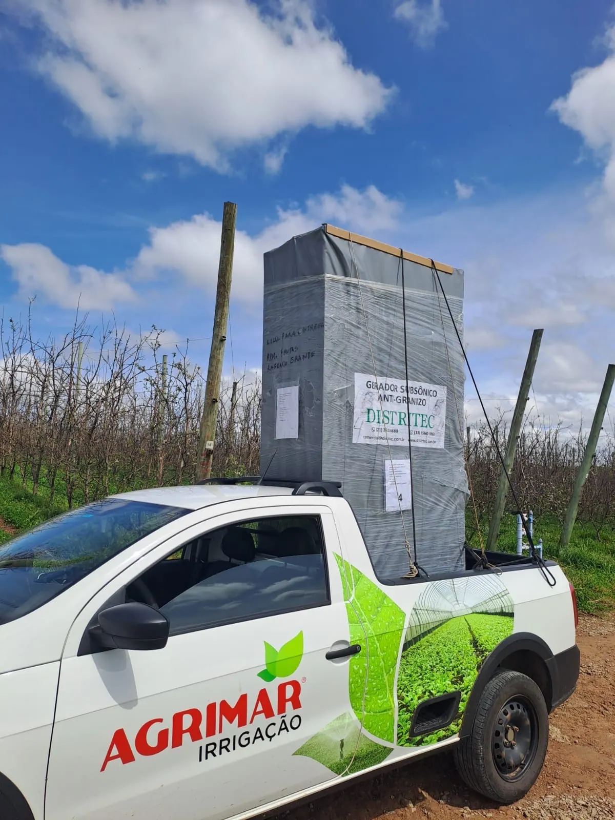 Gerador subsônico DGS-AG com cobertura cinza transportado na caçamba de uma caminhonete, em um pomar